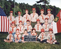 17 scouts and adults dressed in Class A Uniforms in front of a pond.  To the left if the US flag, to the right is the Troop 53 flag.  The sign in front says 