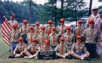18 scouts and adults in Class A uniforms smiling at the camera in front of a pond.  The sign in front says 