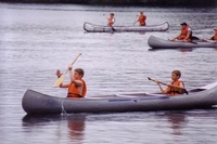 Three canoes are in thie picture, each of which have two people with life jackets on.