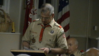 Man in a Class A uniform is reading something from a podium.