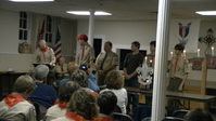 Five people are standing at the front of the room.  All but the one in the middle are wearing Class A uniforms.