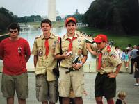 Four scouts standing with the Washington Monument in the background.  The three to the right are wearing Class A uniforms, the scout on the left is wearing a red Class B.
