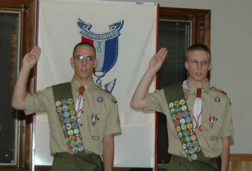 Two Eagle Scouts given the scout sign in front of an Eagle Scout banner.