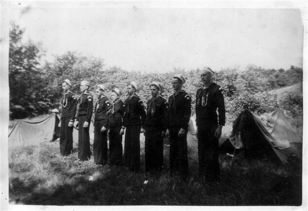 Eight scouts in a line facing towards the left.  There is a tent behind them.