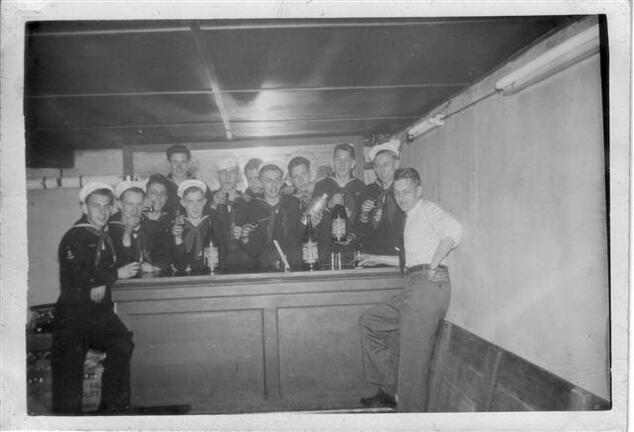 Twelve scouts standing behind a bar inside of a basement.