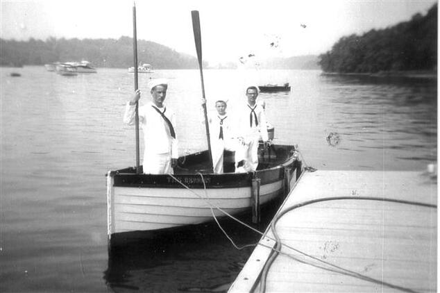 Three scouts standing in a row boat on the Hudson River.  The two on the left are holding up oars.