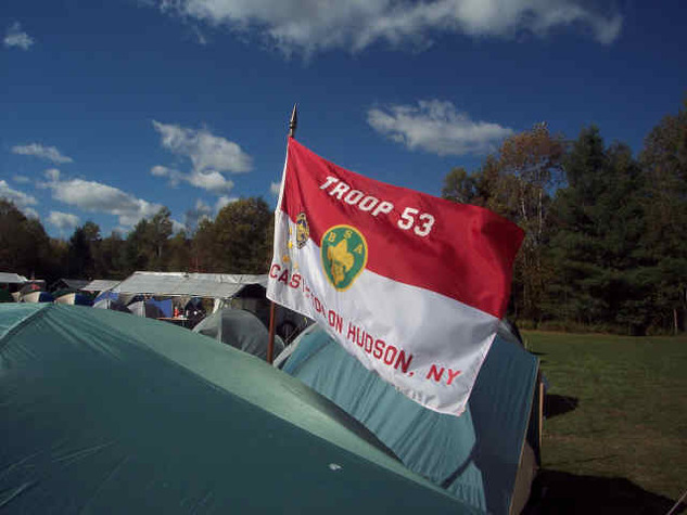 A red and white flag waving in the breeze surrounded by tents.  It says 