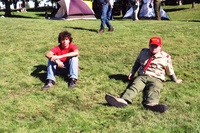 Two scouts sitting on the grass.  The one on the right is wearing a class A.