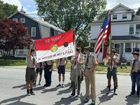 Scouts in Class A uniforms showing off the troop flag.  It is red on the top half and white on the bottom half.  It says 