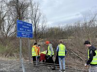 Six scouts picking up trash on the side of the road.  All are wearing reflective yellow vests.  There is a sign that says 