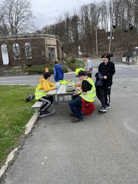 Two scouts wearing reflective yellow bests sitting at a picnic table.  Three scouts are standing around the table.