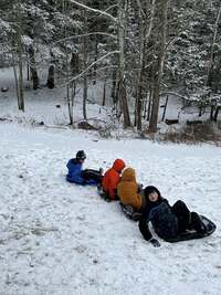 Four scouts sit on sleds about to go down a snowy hill.
