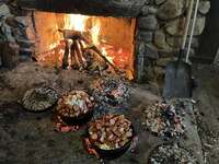 Three dutch ovens are sitting over coals.  There is a fire in a fireplace behind them.