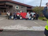 Scouts and scouters are standing in front of a building smiling for the camera.  They are holding 