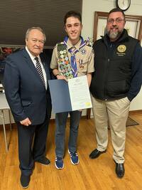 Three people smiling for the camera.  Liam is in the middle holding a Rensselaer County Proclamation.