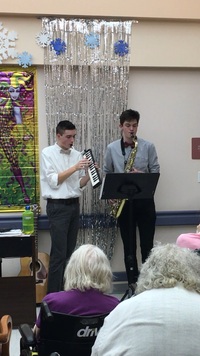 The student on the left playing a melodica, the student on the right playing a saxophone.