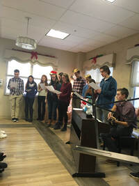 11 Students singing and playing instruments in the front of a room.