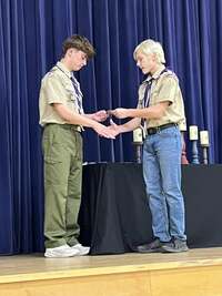 A scout giving an award to another scout.  Both scouts shake hands.