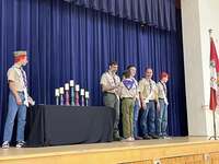 The scoutmaster giving an award to a scout.  He is joined by other adults and scouts standing beside him.