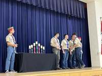 The scoutmaster giving an award to a scout.  He is joined by other adults and scouts standing beside him.