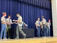 The scoutmaster giving an award to a scout.  He is joined by other adults and scouts standing beside him.