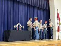 The scoutmaster giving an award to a scout.  He is joined by other adults and scouts standing beside him.