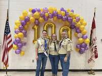 Three people in class A uniforms stand in front of the balloon wall.