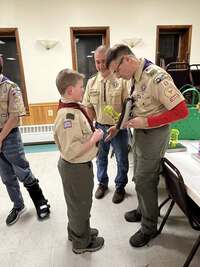 Two adults congratulating a cub scout after crossing over.