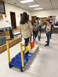 A girl Cub Scout crosses over a small bridge.  One half of the bridge is painted blue and gold, the other side is tan.