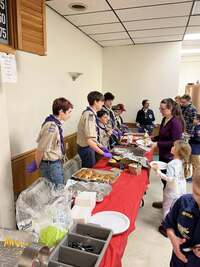 Six scouts help serve dinner.  All are wearing class A's and wearing purple gloves.
