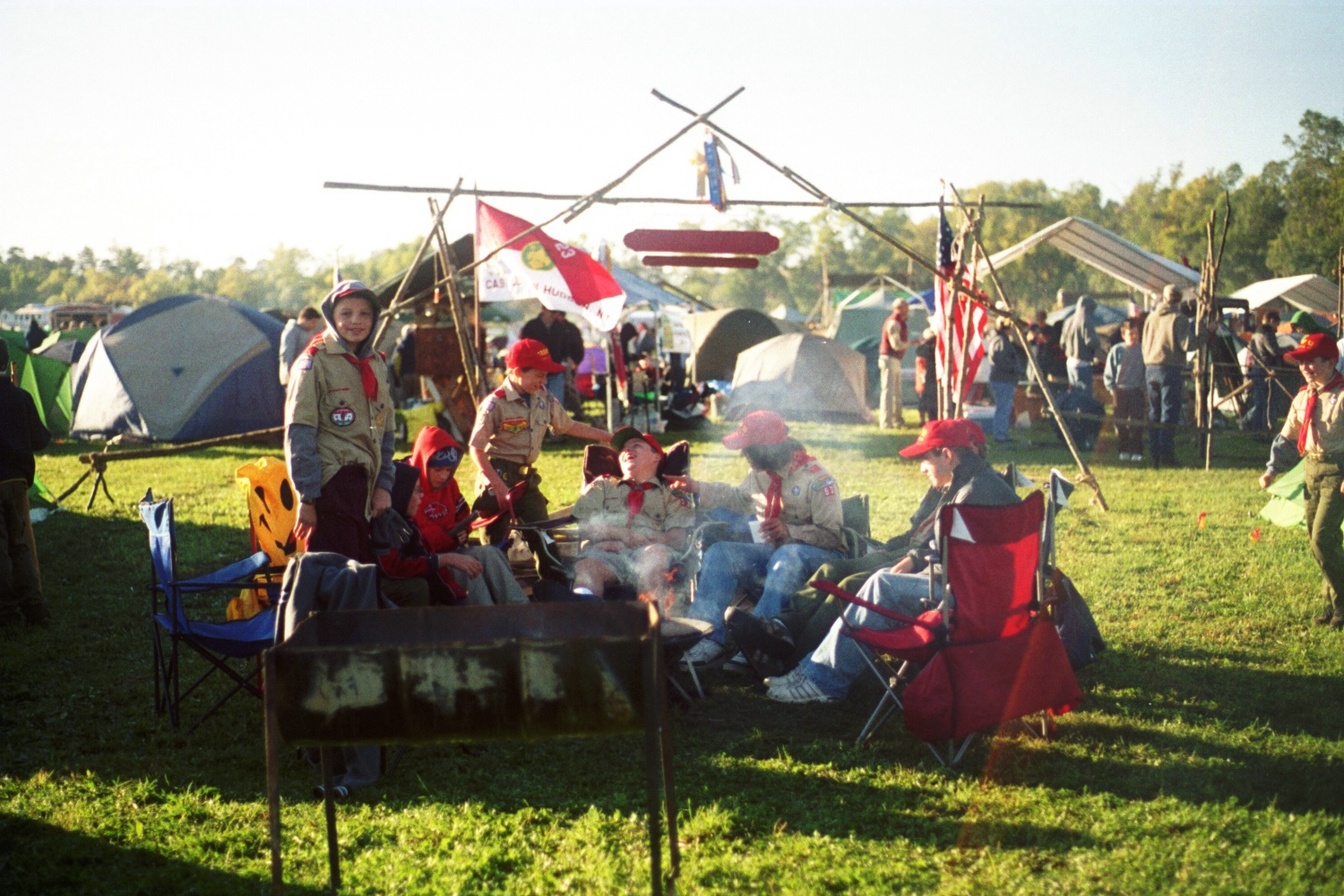 A group of scouts sitting around a campfire.  Many of whom are in class A uniforms.