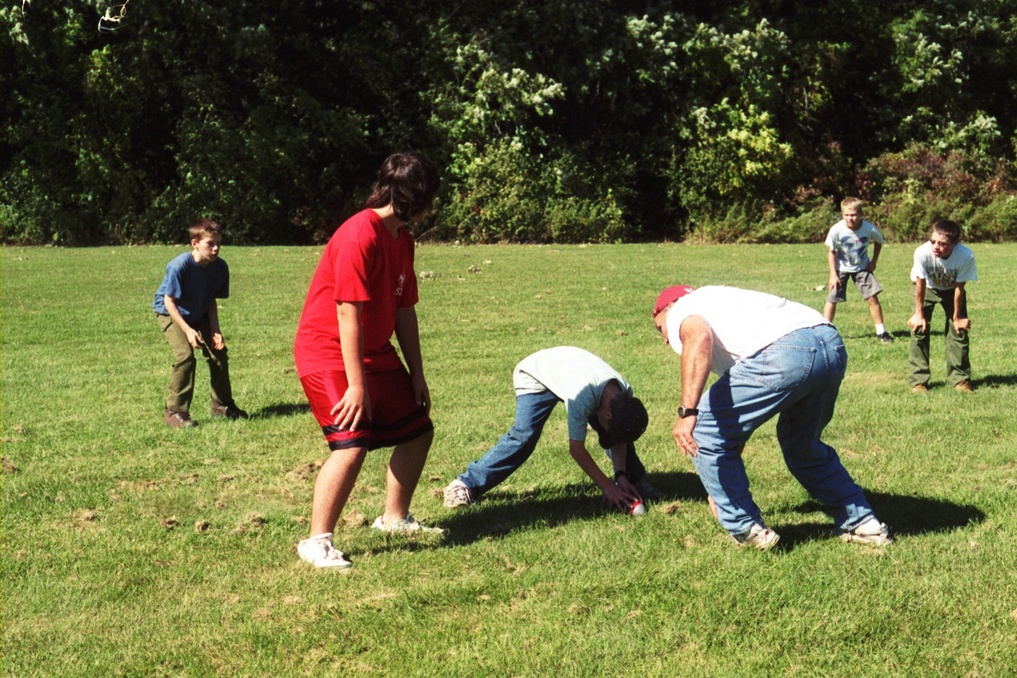 Scouts and an adult playing football in a field.