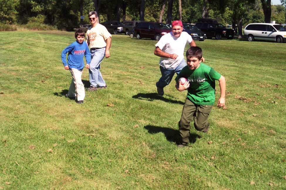 Two scouts and and two adults playing football in a field.