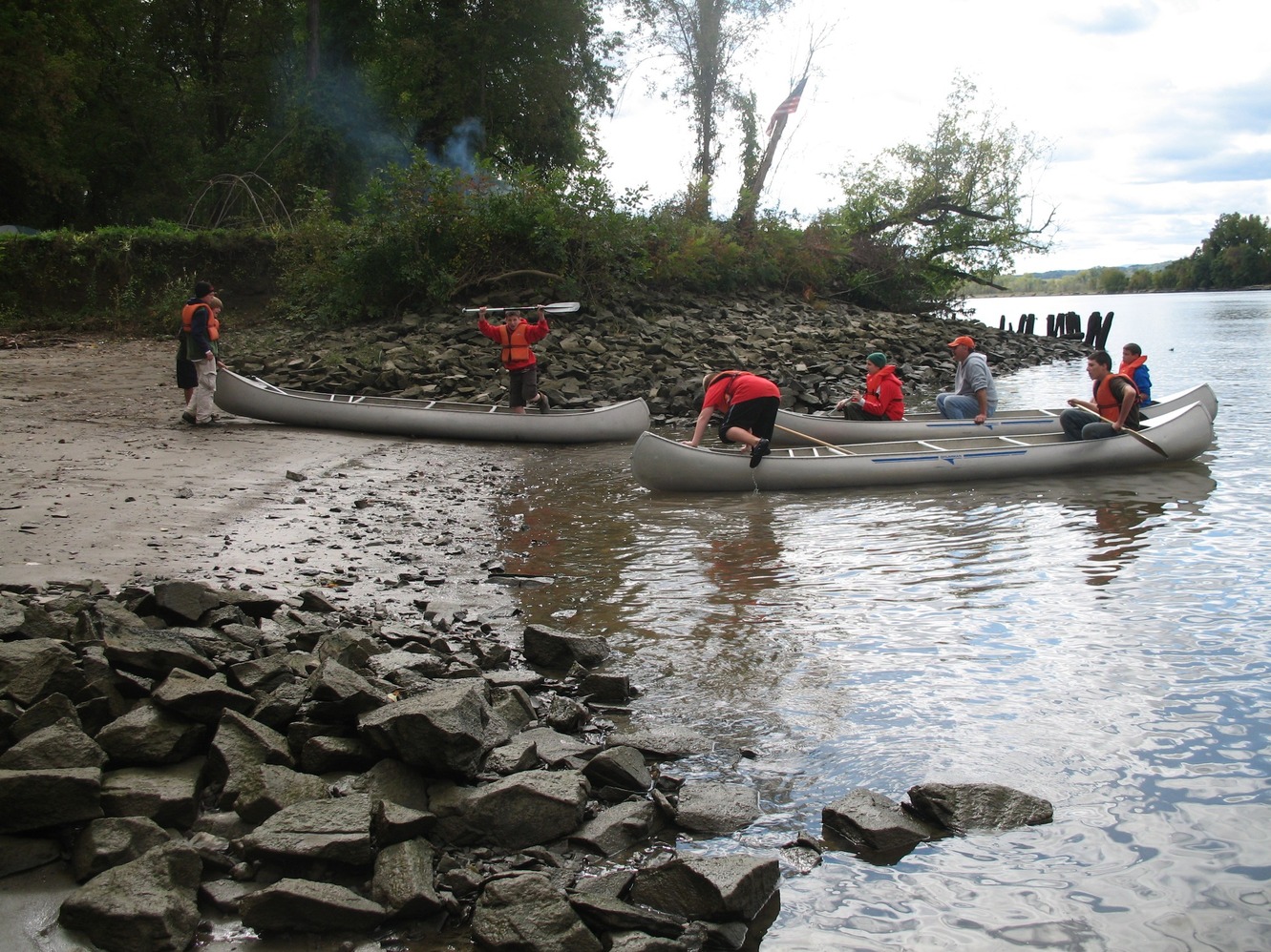 Three canoes full of people arrive on a rocky beach.