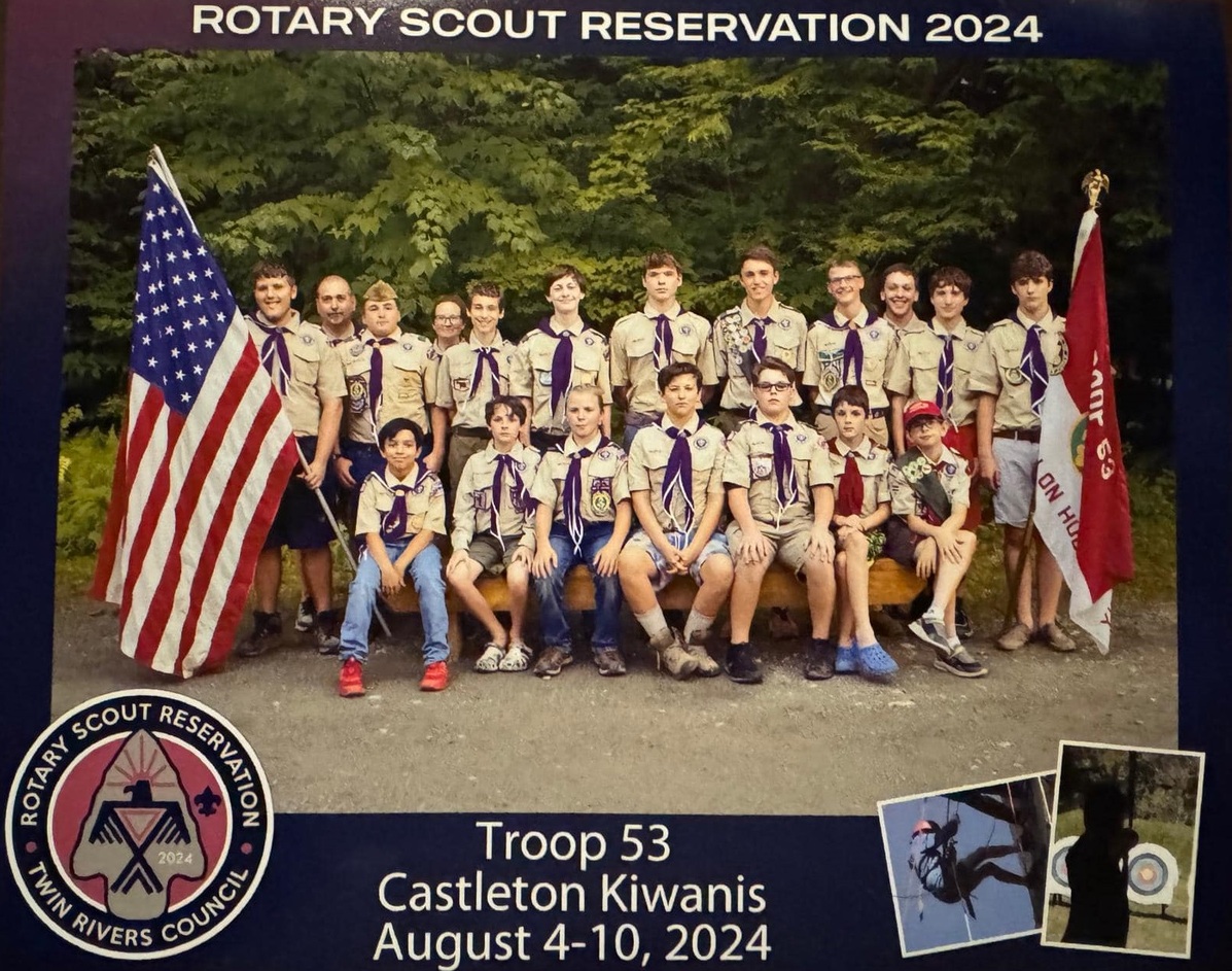 19 people in Class A uniforms smiling for the camera.  To the left is the American flag, and to the right is the Troop flag.  There is text above and below the photo that reads 