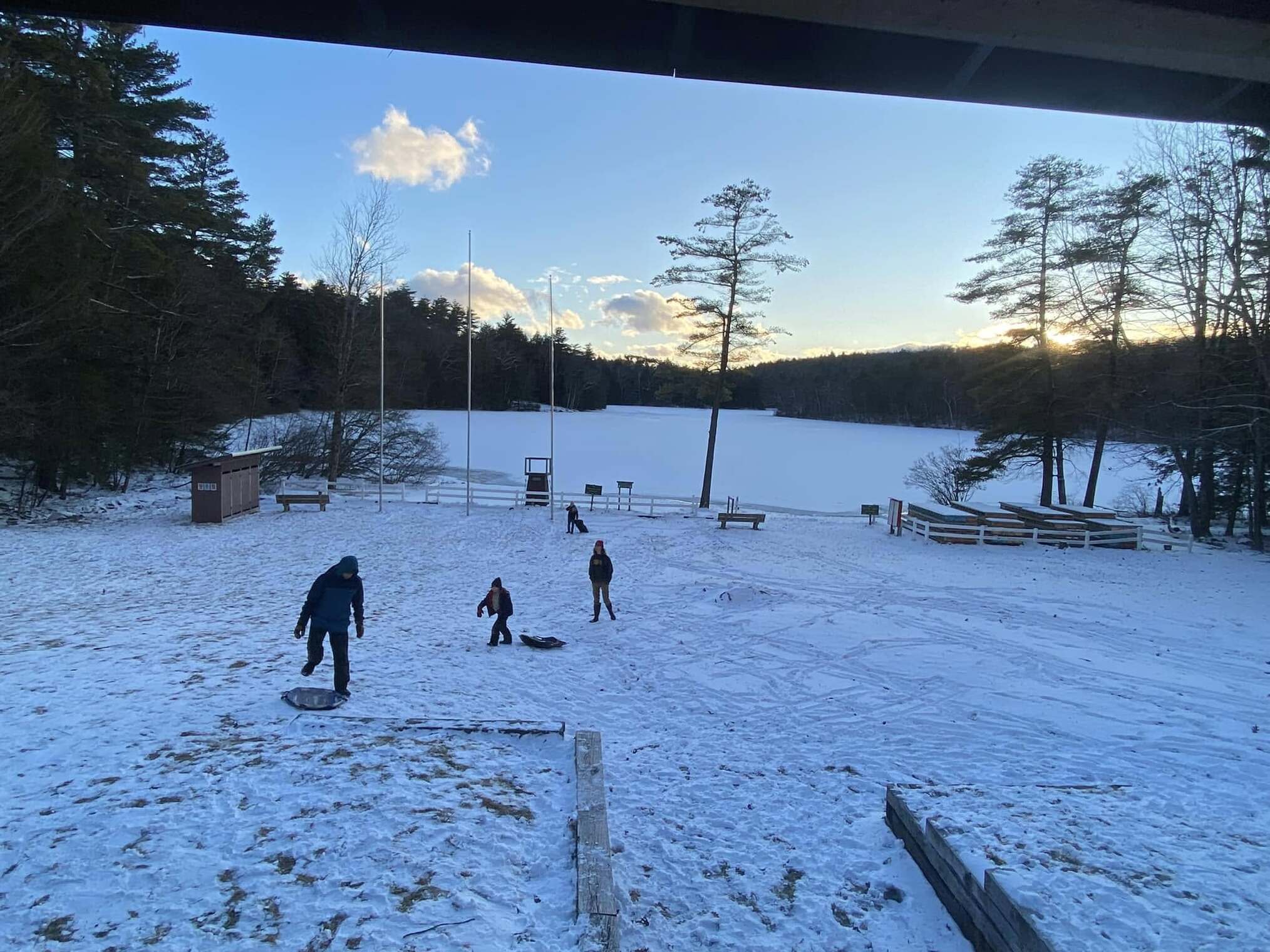 Four scouts sledding down a snowy hill.  There is a frozen lake in the background.