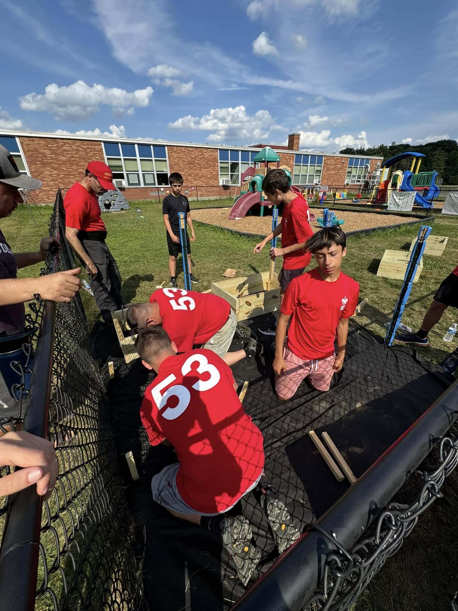 Scouts are assembling the garden boxes on a black tarp.