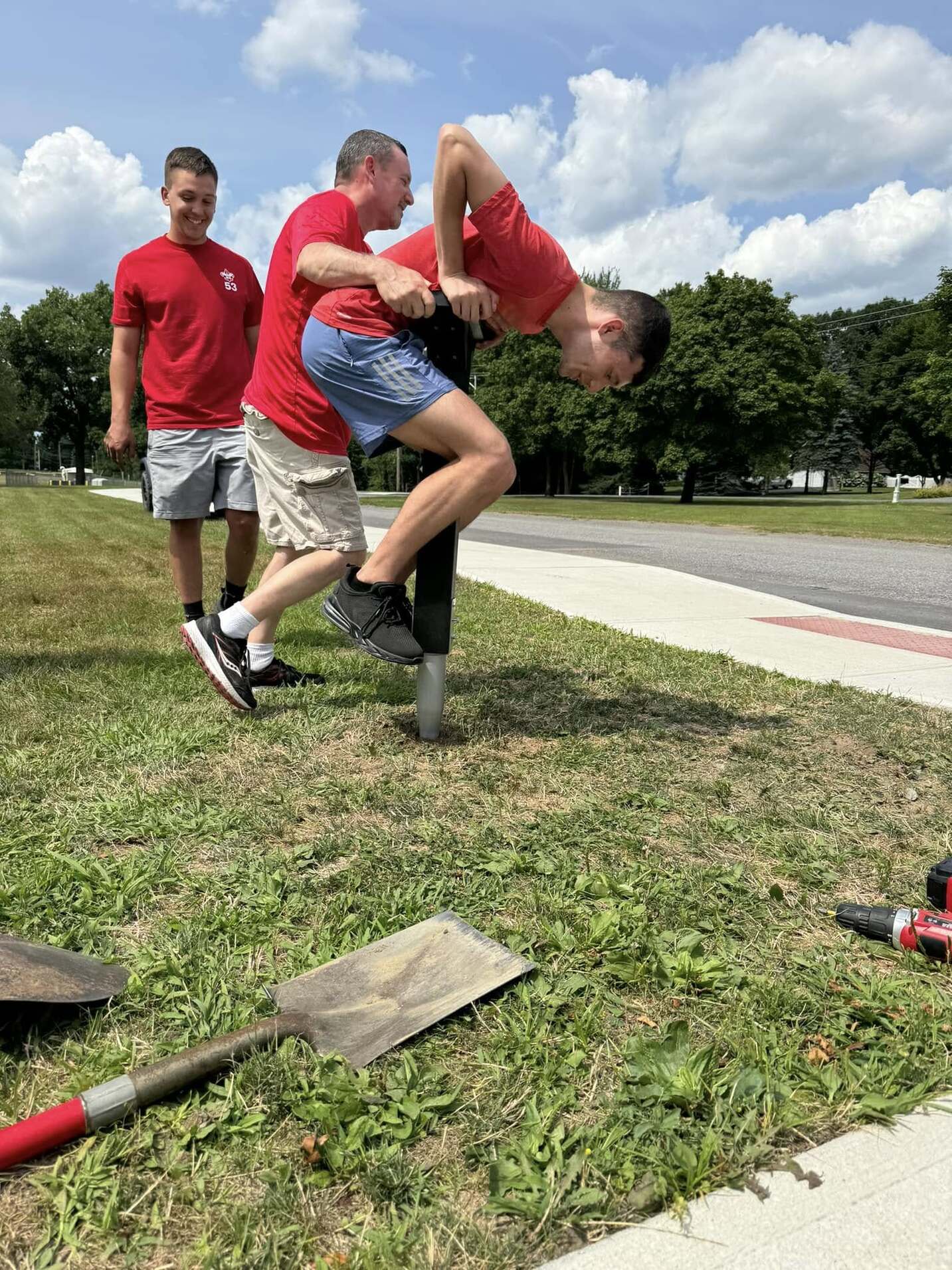 One person is on top of the post trying to get it into the ground.  Another is holding the post steady.