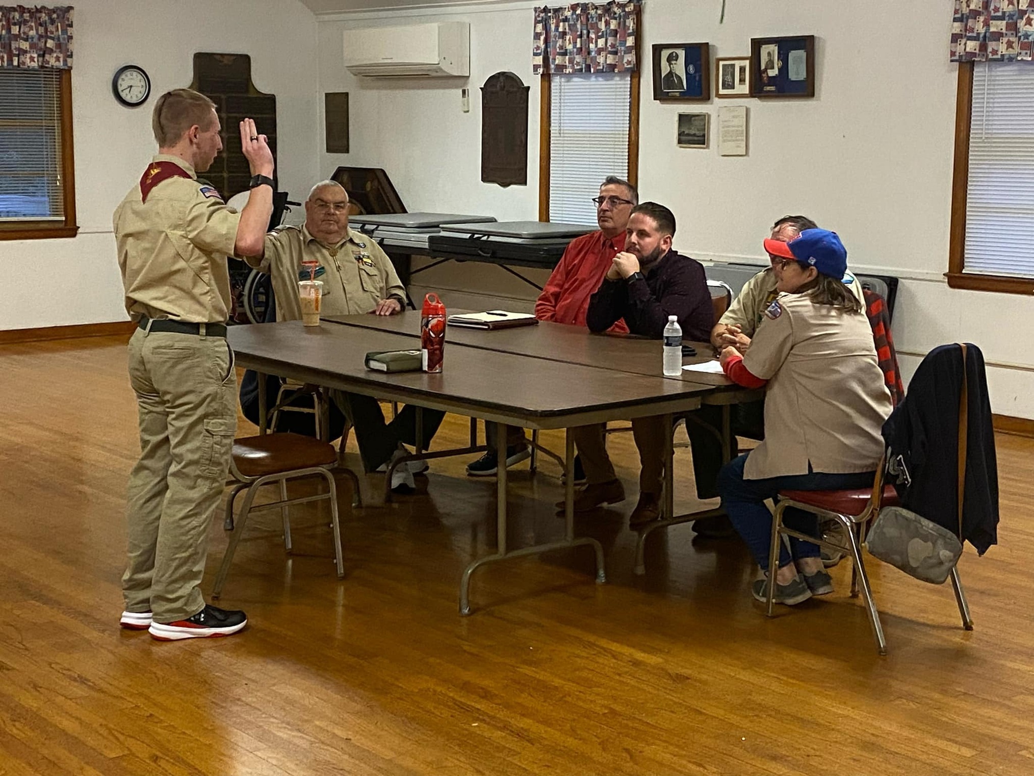 Five people sitting around a table.  Ciaran is standing in front of them with, holding the scout sign.