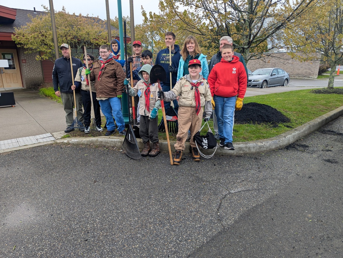 Scouts and Scouters stand on a curb holding shovels and smiling for the camera.