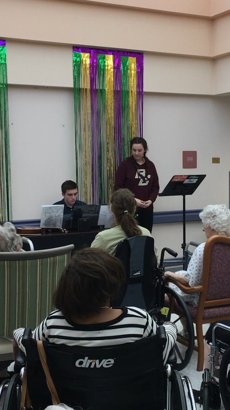 A male student playing the piano, while another female student stands to the right of him.