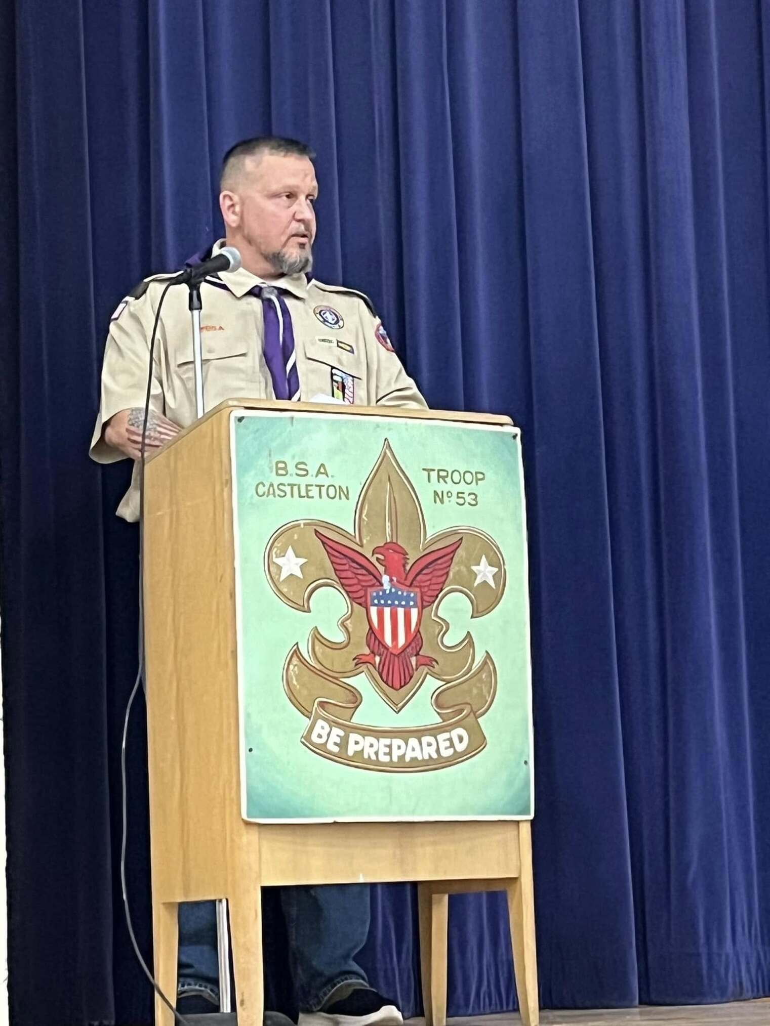 A man in a tan class A uniform speaking into a microphone at a podium.