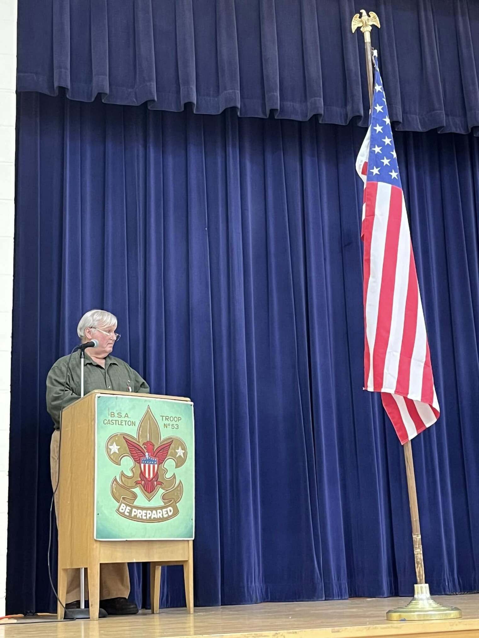 A gray-haired man speaking into a microphone at a podium.