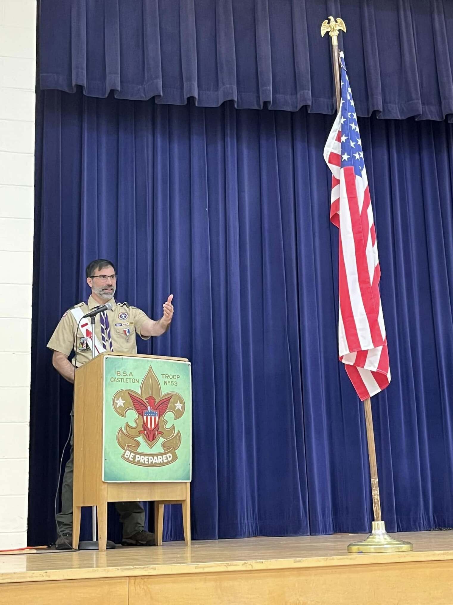 A man in a tan class A uniform speaking into a microphone at a podium.