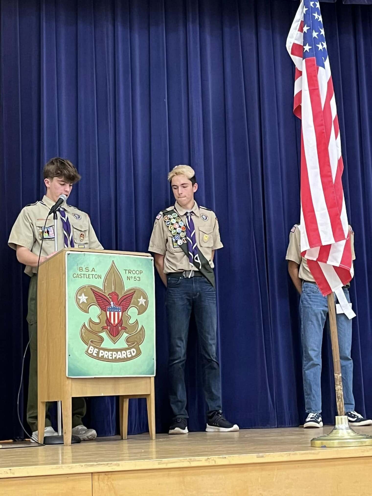 A two scouts in tan class A uniforms speaking into a microphone at a podium.