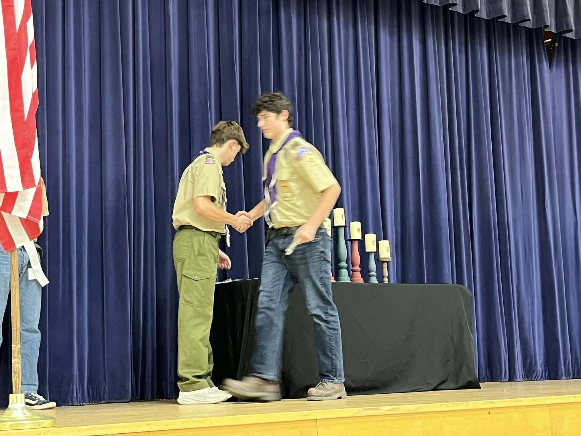 A scout giving an award to another scout.  Both scouts are shaking hands.