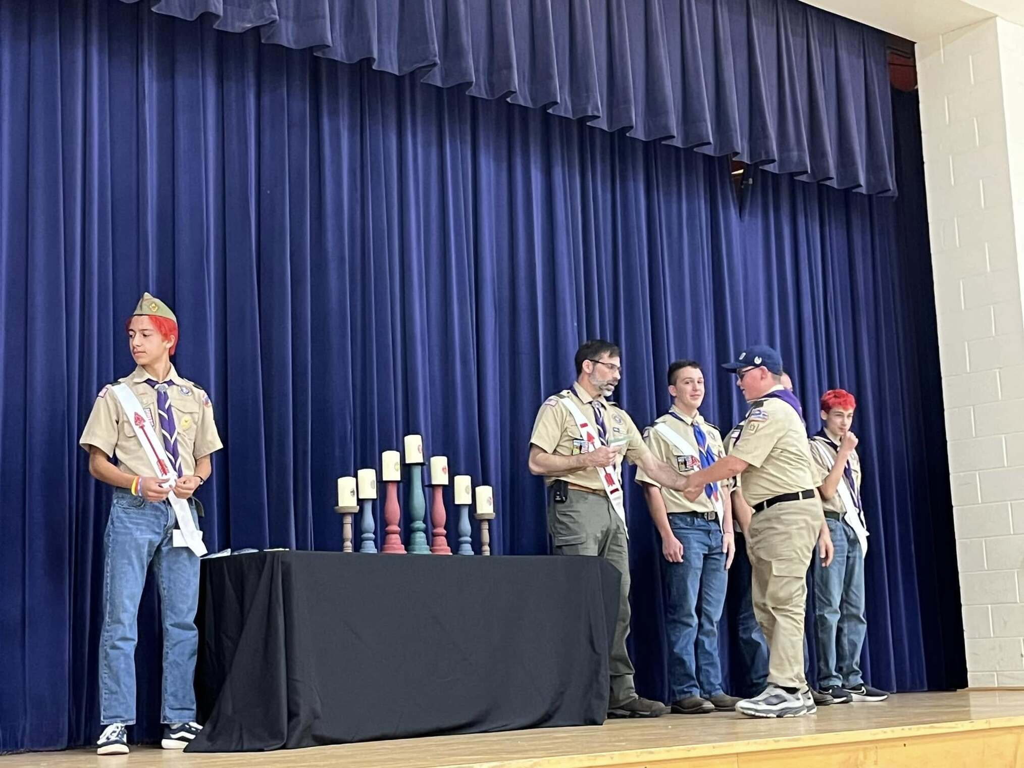 The scoutmaster giving an award to a scout.  He is joined by other adults and scouts standing beside him.