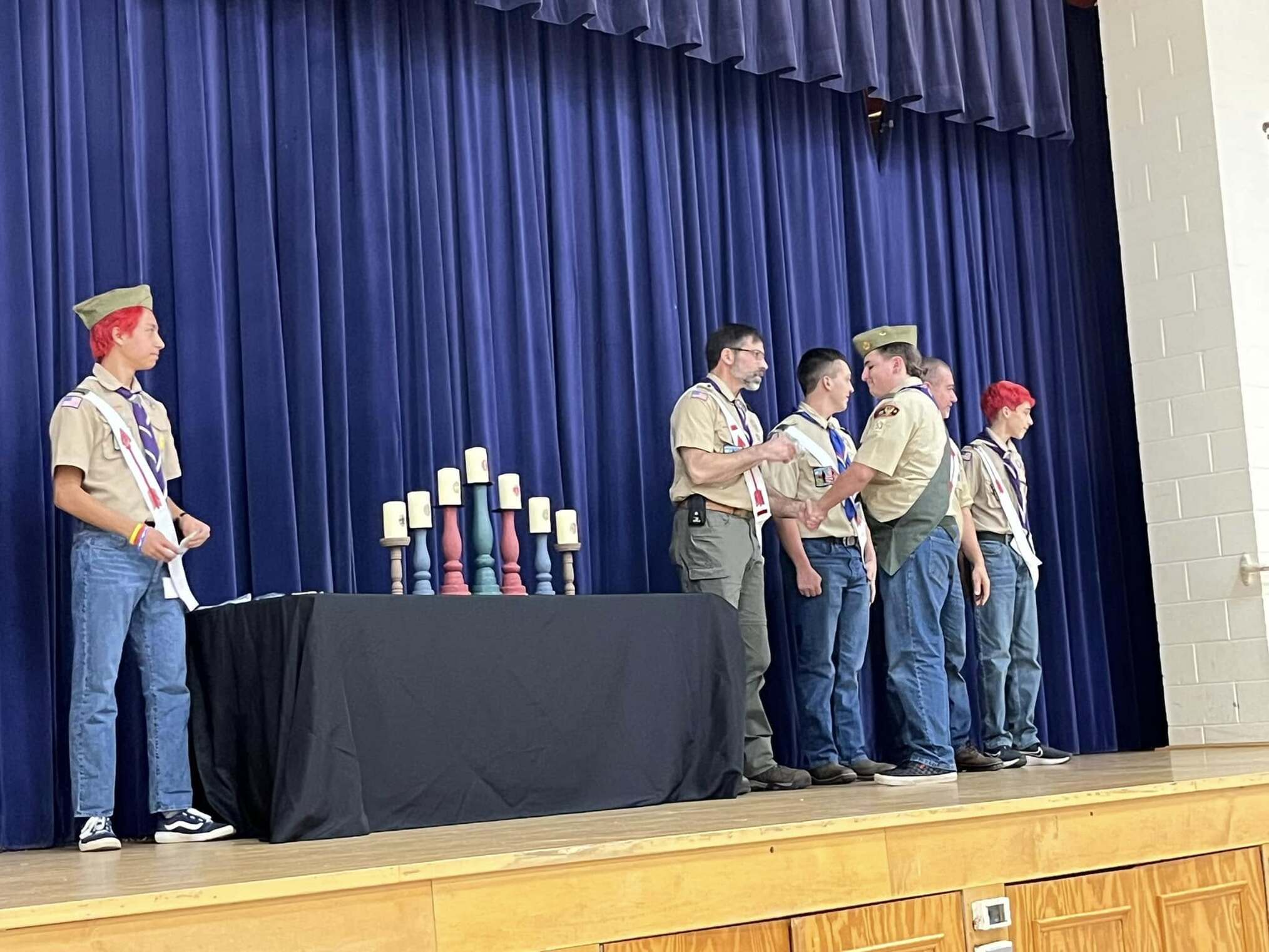 The scoutmaster giving an award to a scout.  He is joined by other adults and scouts standing beside him.