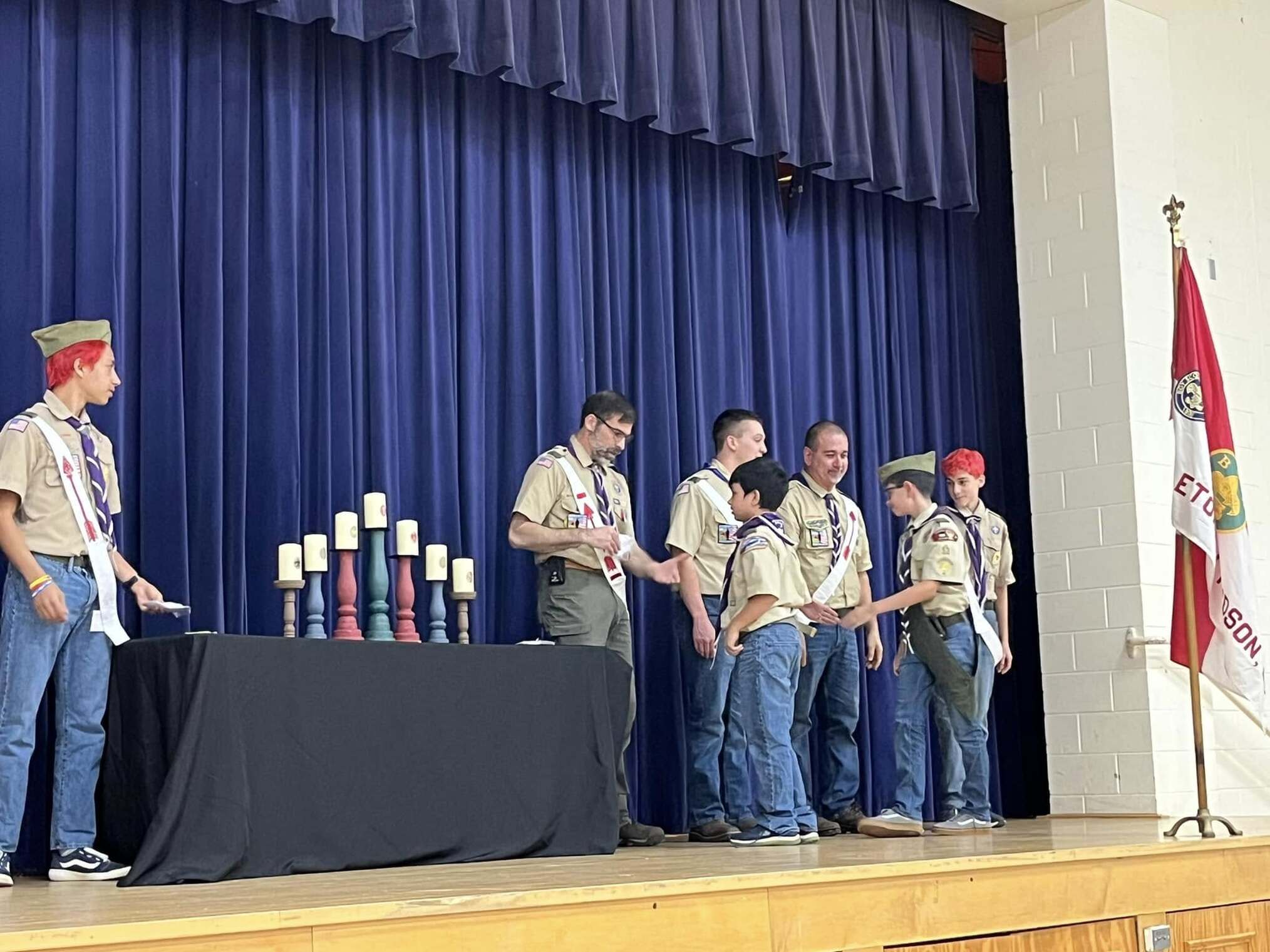 The scoutmaster giving an award to two scouts.  He is joined by other adults and scouts standing beside him.