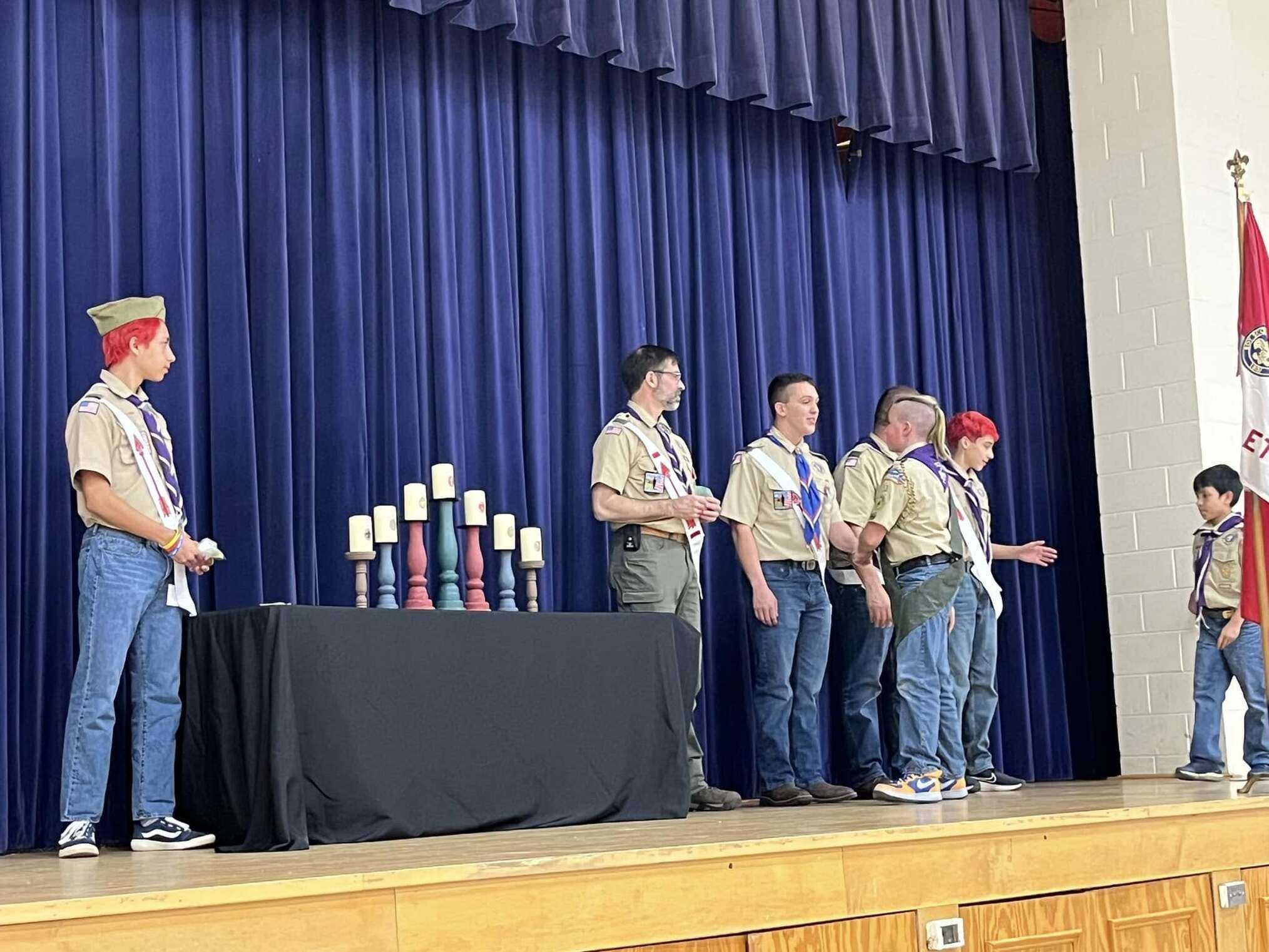 The scoutmaster giving an award to a scout.  He is joined by other adults and scouts standing beside him.